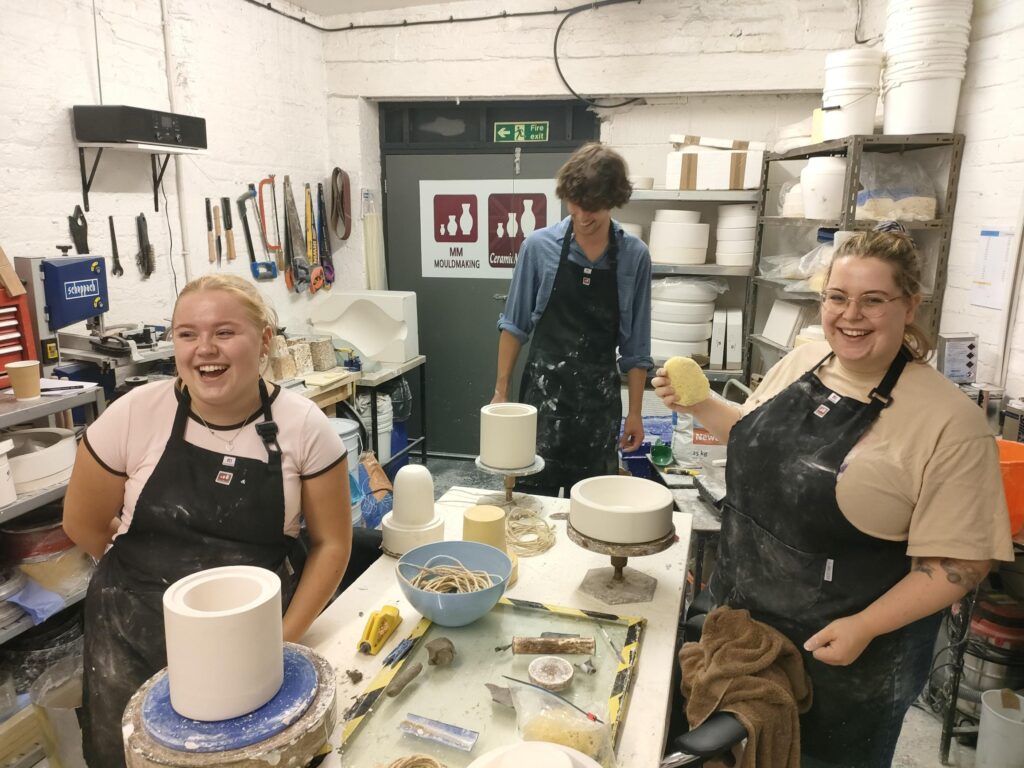 Group of ceramists apprentices showcasing the work they have made from their training.
